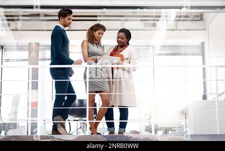 Lets discuss new ideas. a diverse young group of colleagues at work discussing ideas on a tablet in the office. Stock Photo