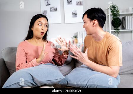 Upset Asian boyfriend and girlfriend sitting together on sofa at home after having quarrel and fight at home. Offended married couple in silence after relationship problem Stock Photo