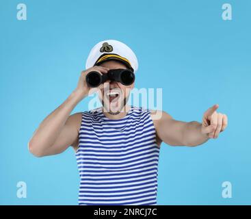 Sailor looking through binoculars and pointing on light blue background Stock Photo