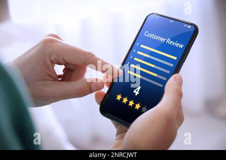 Man using smartphone to give feedback indoors, closeup. Customer review Stock Photo