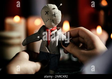 Woman holding voodoo doll with pins indoors, closeup. Curse ceremony Stock Photo