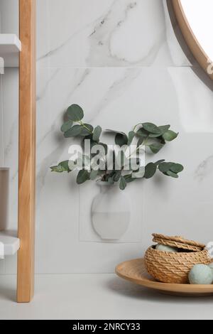 Silicone vase with eucalyptus branches on white marble wall over countertop in stylish bathroom Stock Photo