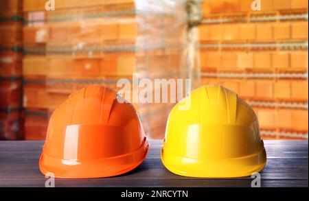 Hard hats on wooden surface near pallets with red bricks Stock Photo