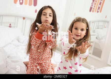 Cute little girls in pajamas playing with feathers on bed at home. Happy childhood Stock Photo