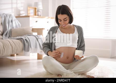 Young pregnant woman with cosmetic product at home Stock Photo