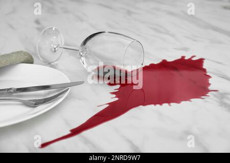 Overturned glass and spilled red wine on white marble table Stock Photo