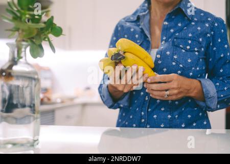 Cut out face portrait with one woman in the kitchen and bananas fruit. Concept of unrecognizable people working at home with food preparing lunch. Rea Stock Photo