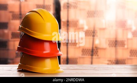 Hard hats on wooden surface near pallets with red bricks. Space for text Stock Photo