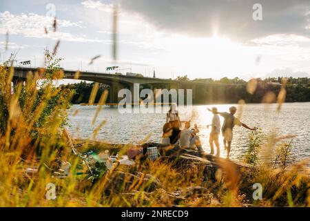 Male and female friends spending leisure time while enjoying picnic near sea at sunset Stock Photo