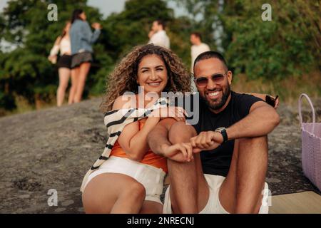 Portrait of happy woman sitting on rock with man wearing sunglasses during picnic Stock Photo