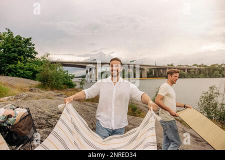 Happy man laying blanket while standing on rock during picnic Stock Photo