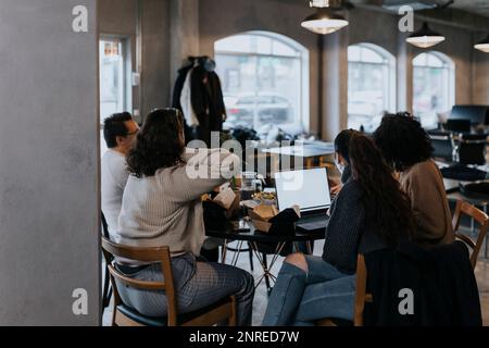 Young programmer working on laptop by male and female colleagues having lunch at startup company Stock Photo