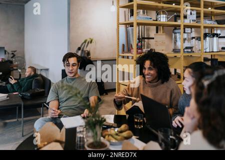Smiling business colleagues discussing while having lunch at table in creative office Stock Photo