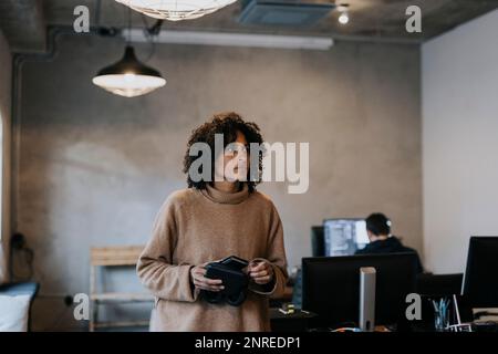Contemplative businesswoman with smart phone looking away while walking in office Stock Photo