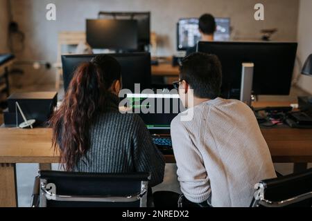 Rear view of young male and female colleagues coding together on laptop at startup company Stock Photo
