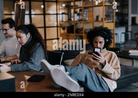 Businesswoman using smart phone by male and female colleagues working at office Stock Photo