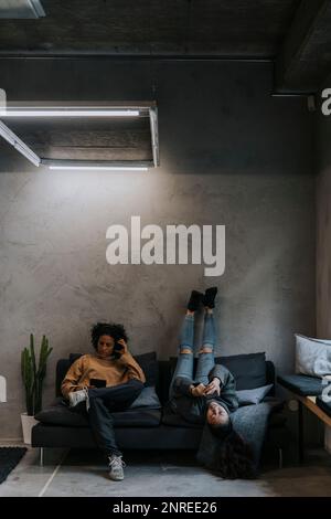 Multiracial female colleagues using smart phones on sofa in creative office Stock Photo