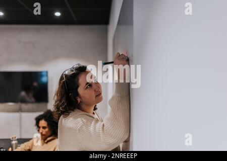 Young businesswoman writing on adhesive note over whiteboard at workplace Stock Photo