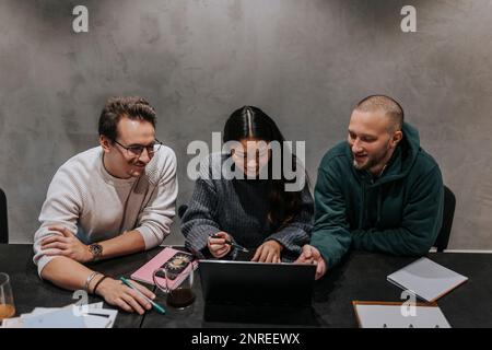 Smiling businesswoman discussing strategy over laptop with male colleagues at workplace Stock Photo