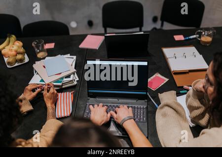Male hacker using laptop amidst female colleagues in board room at creative workplace Stock Photo