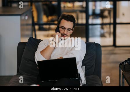 Young businessman talking on mobile phone while working over laptop in creative office Stock Photo