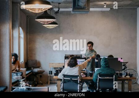 Multiracial female hacker giving pencil to male colleague by computers at desk in office Stock Photo