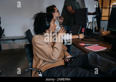 Businesswoman drinking coffee while looking at computer hacker working in startup company Stock Photo