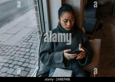 Young businesswoman using mobile phone by window at office Stock Photo