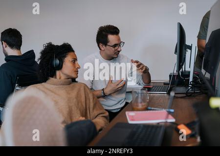 Young male programmer explaining strategy to female colleague by computer at desk in office Stock Photo