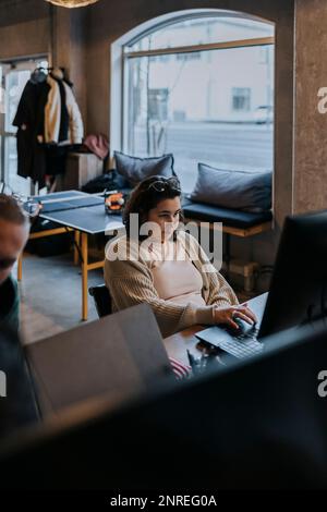 Young female hacker working on laptop by male colleague in startup company Stock Photo