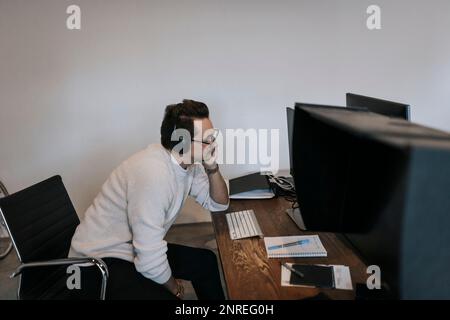 Businessman with hand on chin working over computer at desk in creative office Stock Photo