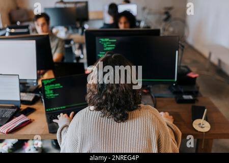 Rear view of young female programmer coding on computer at desk in office Stock Photo