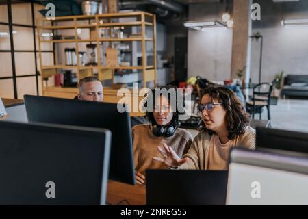 Young female hacker explaining strategy to colleagues over computer while working in office Stock Photo