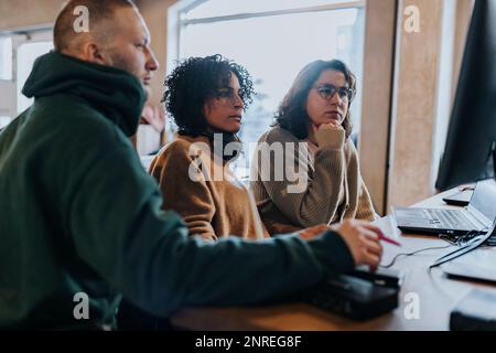 Multiracial female and male hackers discussing over computer at desk in startup company Stock Photo