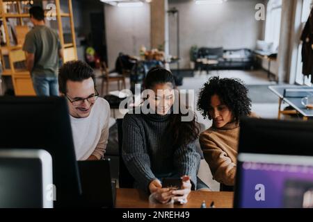 Smiling female entrepreneur sharing smart phone with colleagues in startup company Stock Photo