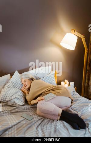 Senior woman sleeping on bed near illuminated lamp at home Stock Photo
