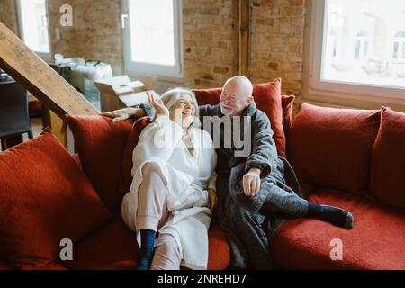 Happy senior couple spending leisure time while sitting on sofa at home Stock Photo