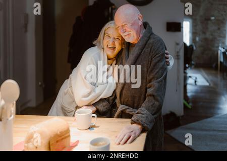 Happy senior woman embracing man wearing bathrobe at home Stock Photo