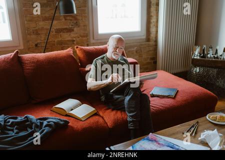 Senior man painting while sitting on sofa at home Stock Photo