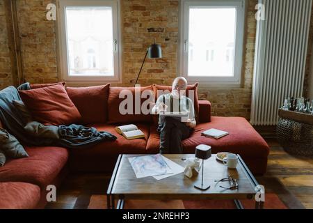 Senior man doing painting while sitting on sofa in living room at home Stock Photo