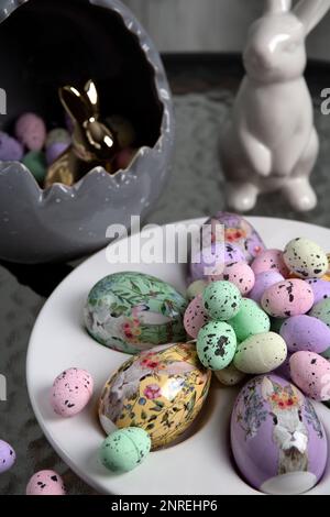 photo of a rabbit sitting in an egg with small eggs inside a large rabbit standing next to a plate of large colored eggs on a glass table Stock Photo
