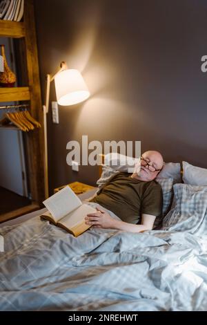 Senior man with book taking nap while lying on bed at home Stock Photo