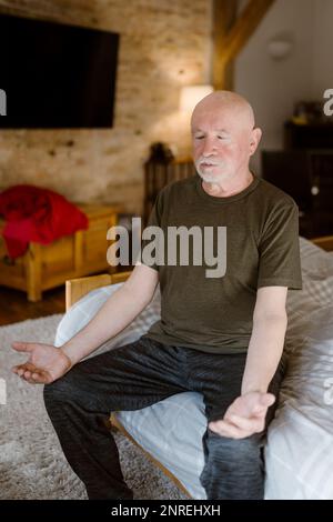 Senior man practicing yoga while sitting on bed at home Stock Photo