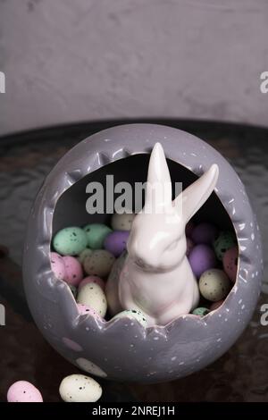photo in a large gray decorative egg is a lot of multi-colored decorative small eggs and sits a white rabbit Stock Photo