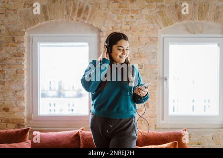 Smiling woman enjoying listening to music through headphones at home Stock Photo
