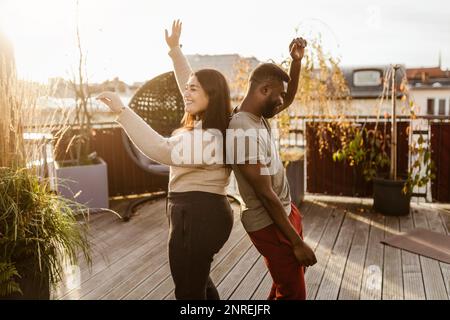 Side view of carefree couple dancing while standing back to back at terrace Stock Photo