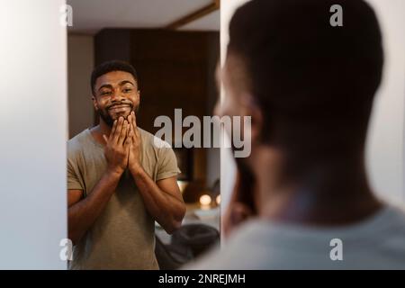 Smiling young man touching face while looking in mirror at home Stock Photo