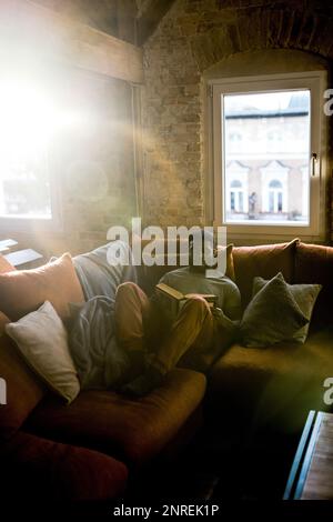 Man spending leisure time while reading book on sofa at home Stock Photo