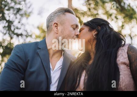 Back lit mature groom kissing young bride during wedding Stock Photo