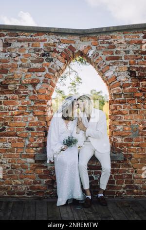 Smiling groom and bride sitting face to face on window sill in wedding Stock Photo